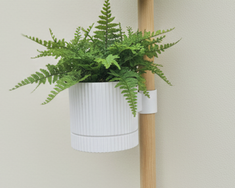 Vertical plant stand with three potted plants against a plain wall.