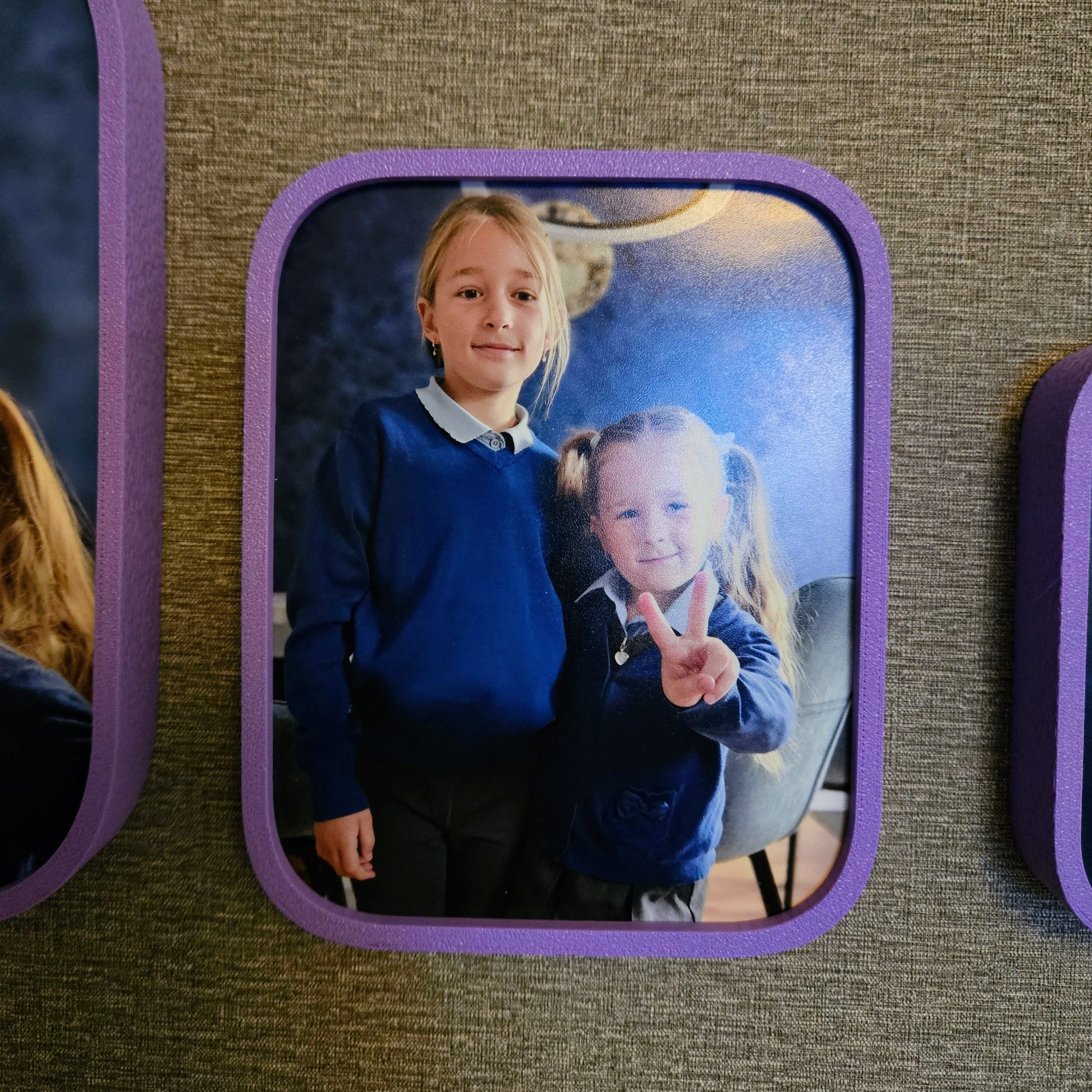 Two children in school uniforms standing together, framed by purple borders on a textured wall.
