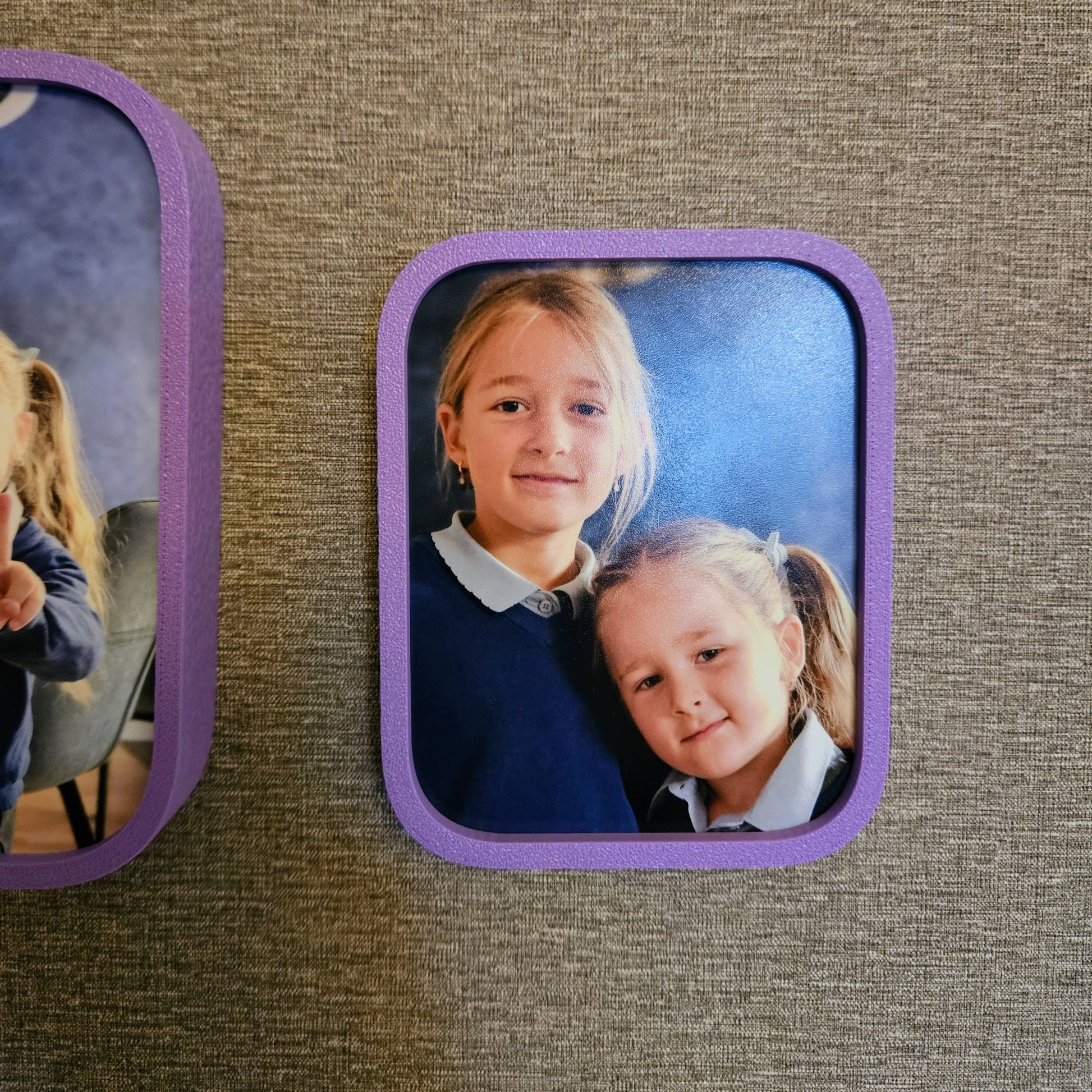Two rectangular photo frames with children's portraits on a textured brown surface.