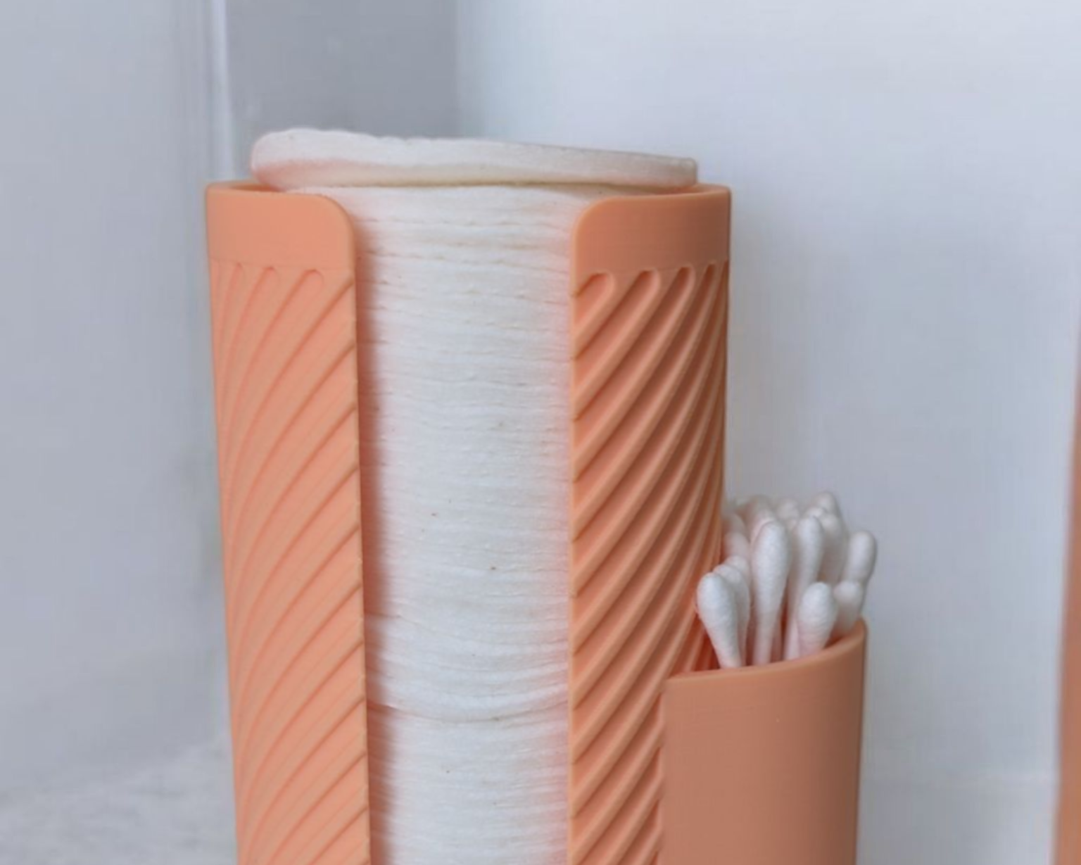 Coral-colored holder with compartments for cotton swabs and cotton balls on a white background