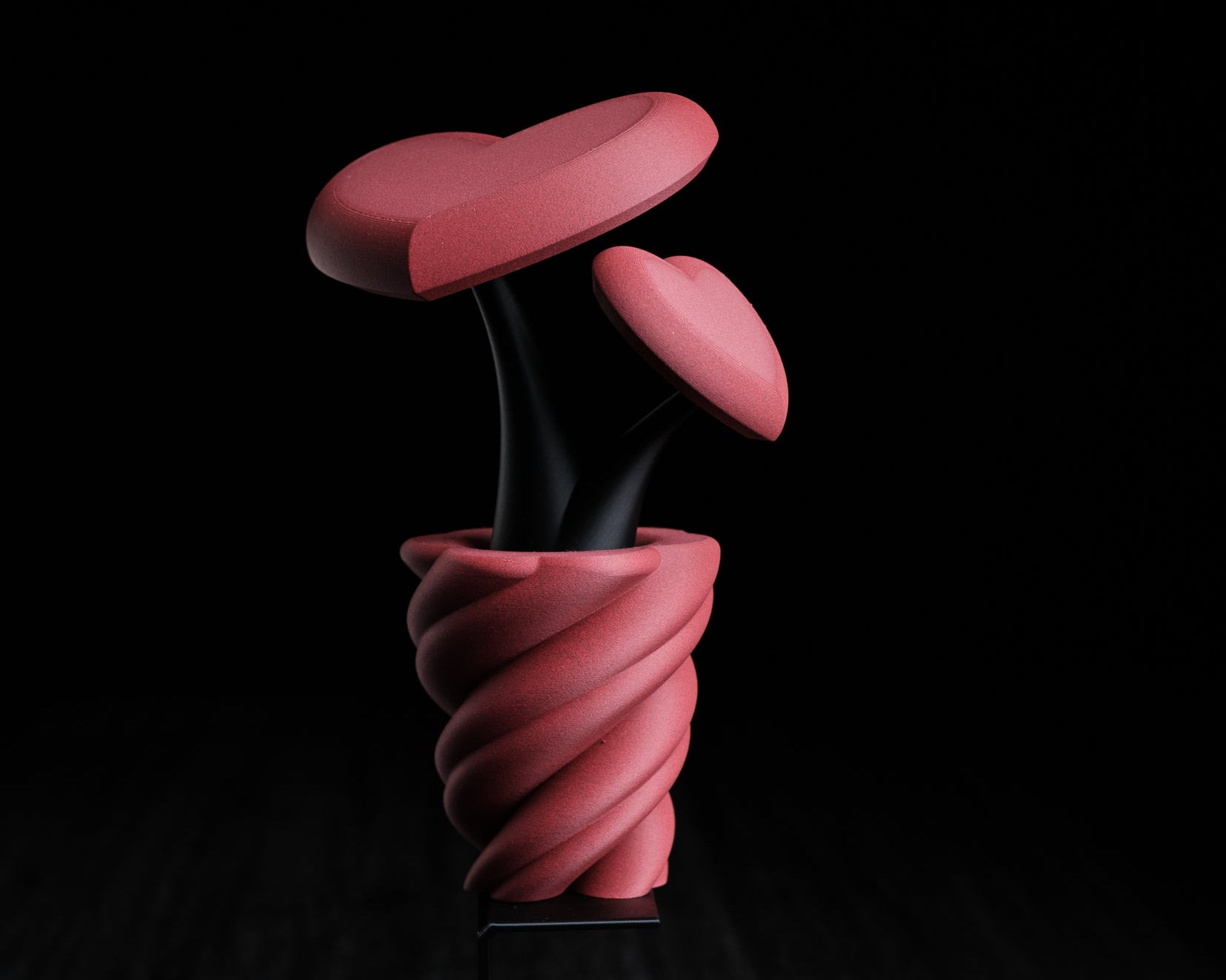 Pink abstract sculpture on a black background with 'h3io design' logo.