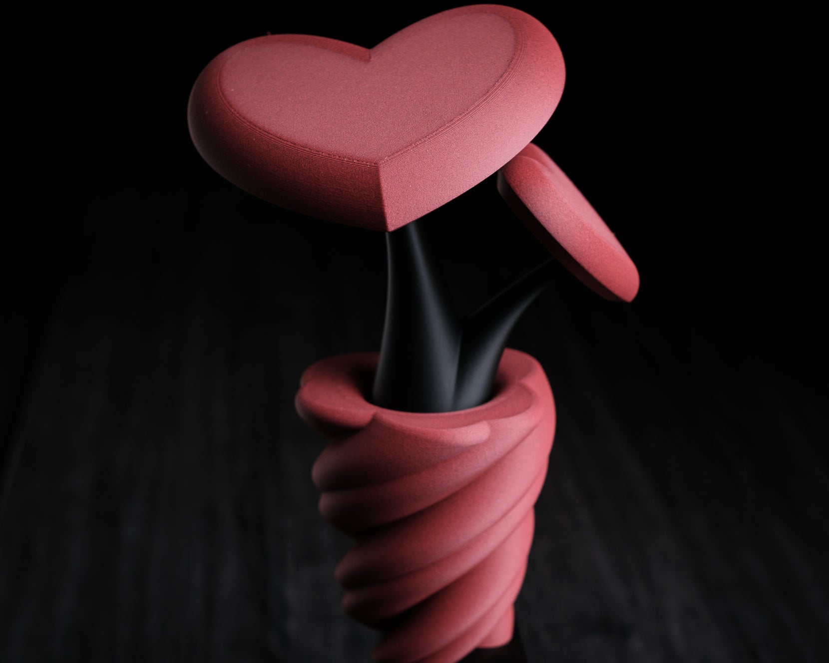Pink heart-shaped object with a black stem on a dark background