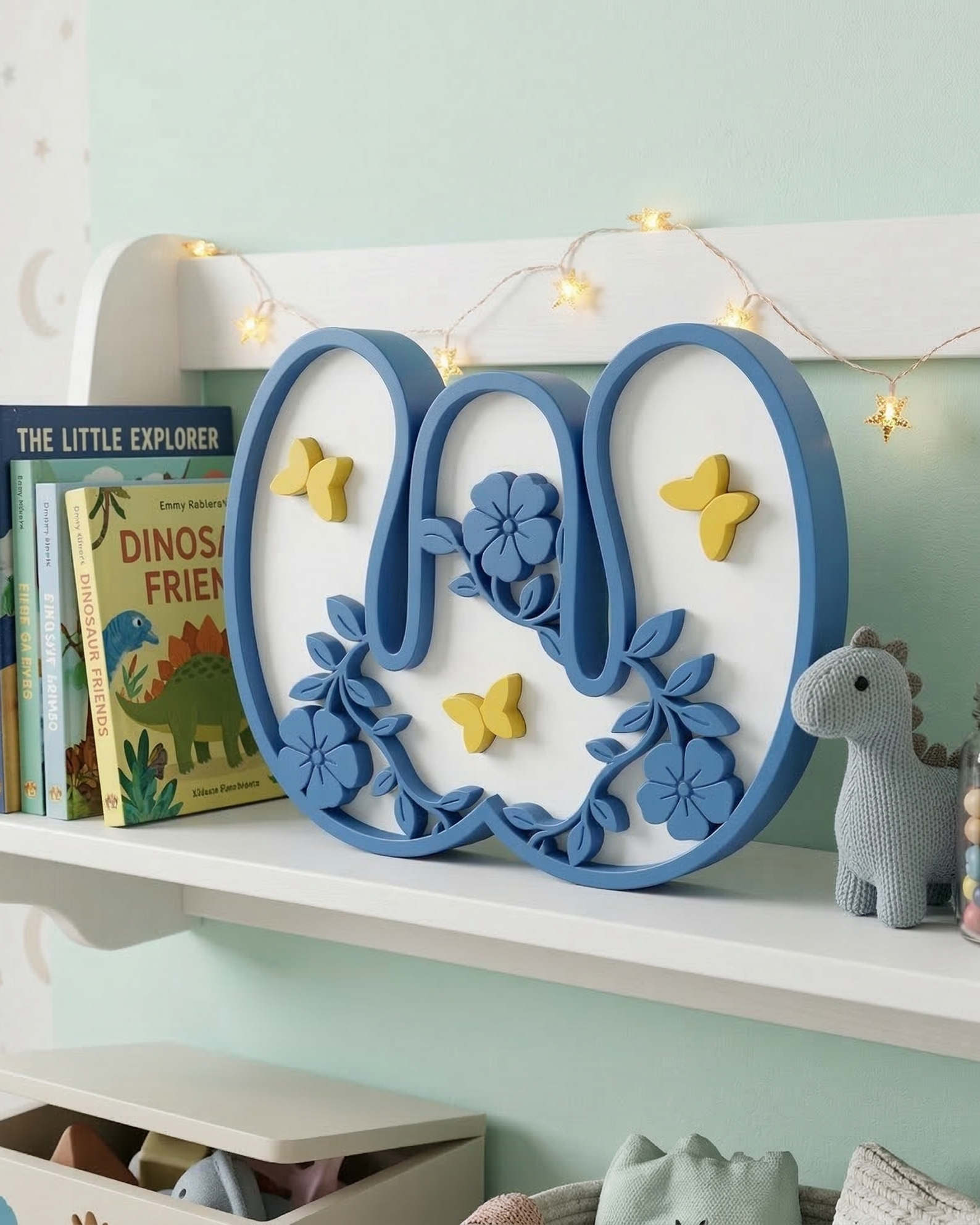 Decorative letter 'W' with floral and butterfly design on a shelf with books and toys.
