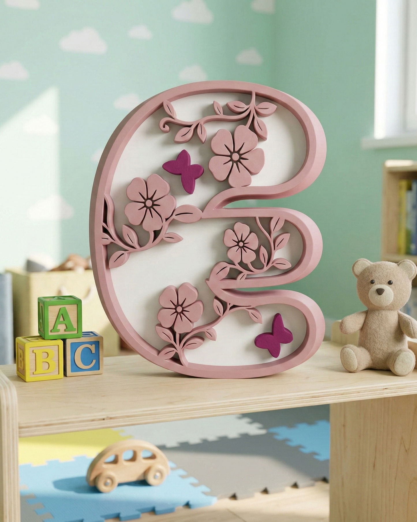 Decorative letter 'E' with floral and butterfly designs on a shelf with toys and blocks.
